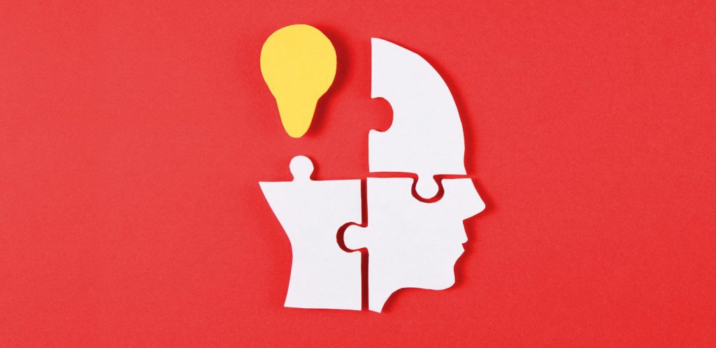 red background with a white head puzzle piece with one yellow lightbulb in the upper left